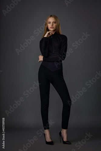 beautiful girl blonde teenager in black clothes posing in the studio on a dark background
