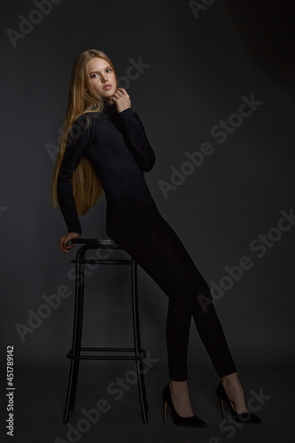 beautiful girl blonde teenager in black clothes posing in the studio on a dark background