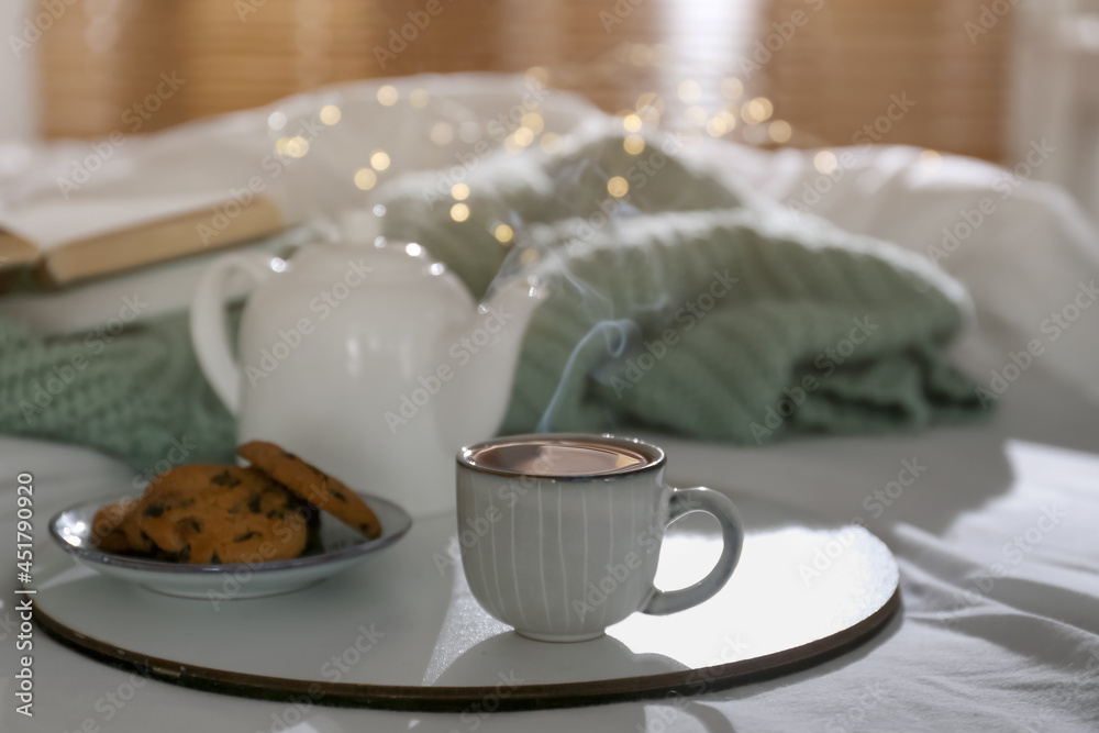 Tray with cup of hot tea, cookies and teapot on bed indoors Tray with cup of hot tea, cookies and teapot on bed indoors