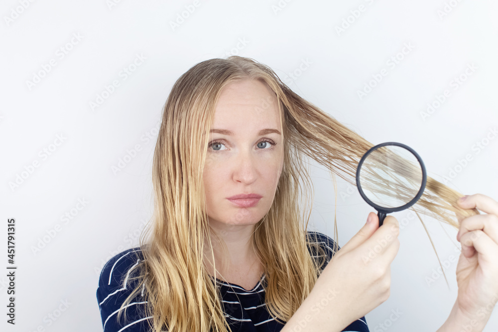 The girl looks in front of the magnifier at her oily hair. Problematic scalp and increased secretion of the sebaceous glands. Hair care. Oily hair care and treatment concept The girl looks in front of the magnifier at her oily hair. Problematic scalp and increased secretion of the sebaceous glands. Hair care. Oily hair care and treatment concept