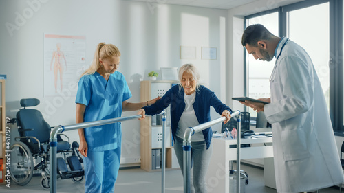 Hospital Physical Therapy: Portrait of Strong Senior Female Patient with Injury Successfully Walks Holding Parallel Bars. Physiotherapist, Rehabilitation Doctor, Help, Assist Disabled Patient