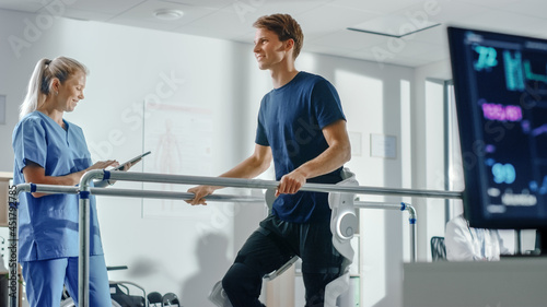 Modern Hospital Physical Therapy: Doctor Uses Tablet Computer, Helps Disabled Patient with Injury Walk on Treadmill Wearing Advanced Robotic Exoskeleton Legs. Physiotherapy Rehabilitation Technology