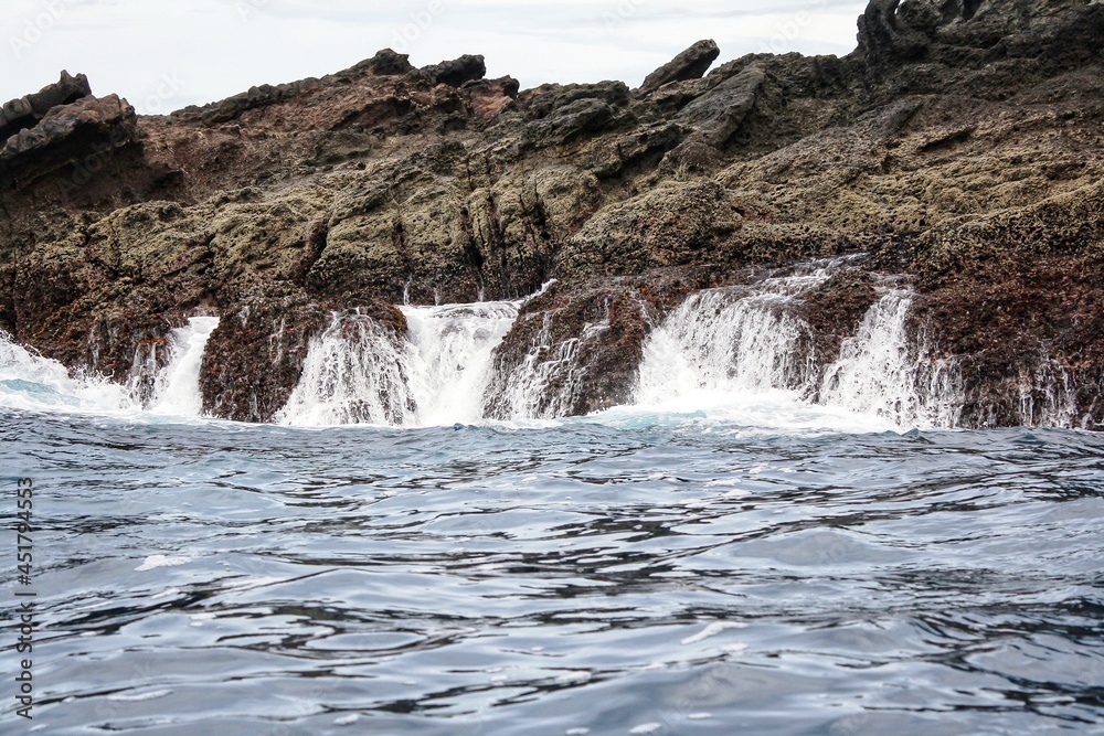 Scenic view of tropical rocky island in sea. Water splash and flowing motion. For environment and geology background. No people. Scenic view of tropical rocky island in sea. Water splash and flowing motion. For environment and geology background. No people.