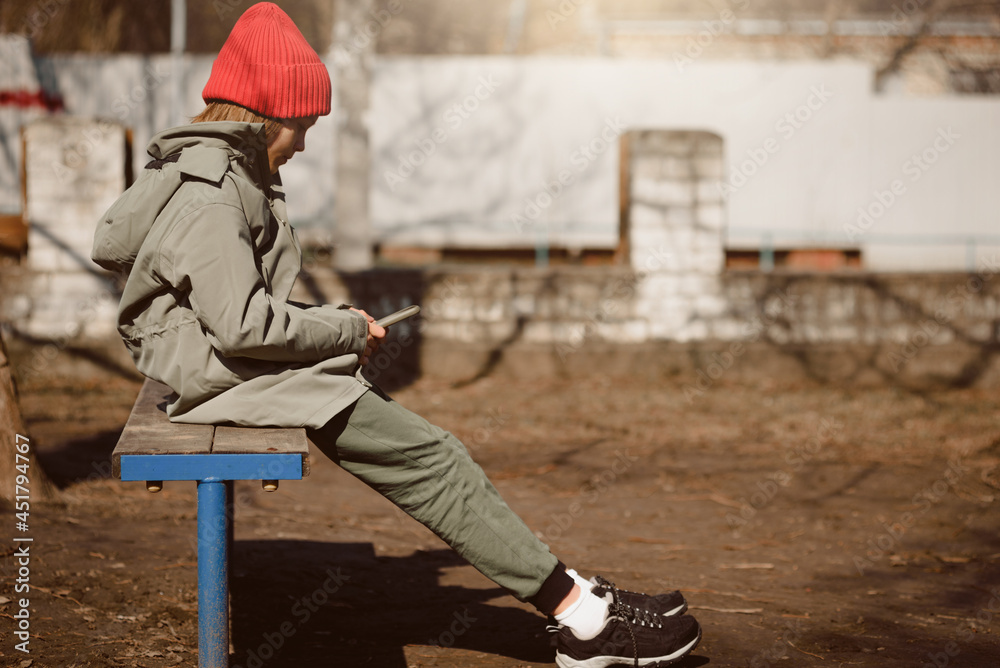 Young addicted teenager looking in smartphone while sitting on bench outdoor