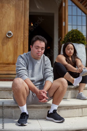 Young biracial couple with Down Syndrome in active wear sitting next to each other and tying shoes