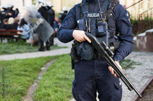 Rifle in the hands of a policeman (inscription in Polish "Police") in the background people and other policemen.