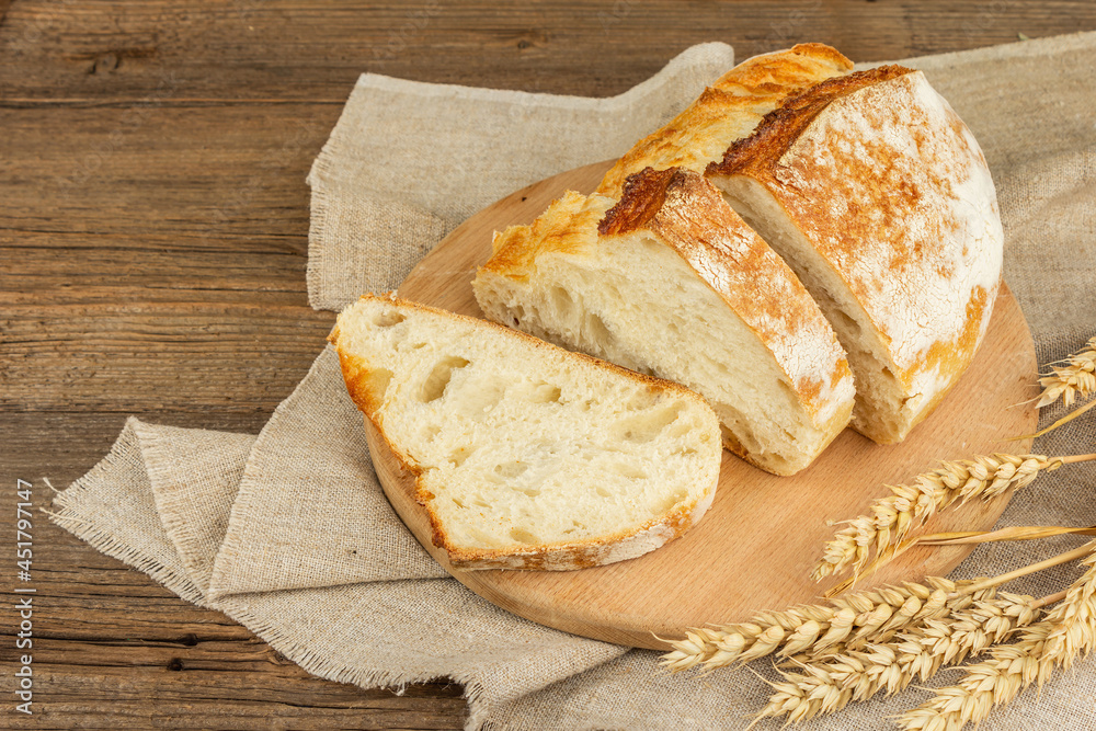 Freshly baked bread with wheat ears, fragrant pieces on a cutting board