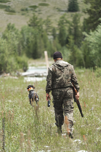 A hunter with a dog walks through a forest glade and holds a rifle in his hands.