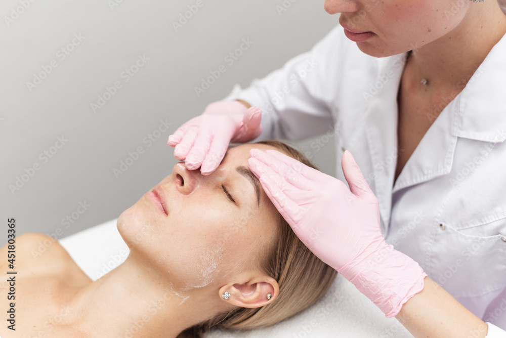 Woman beautician cleans and moisturizes patient's skin in spa salon
