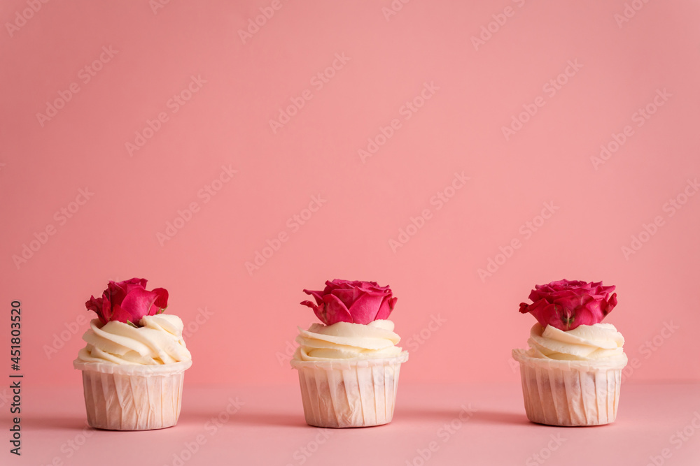 Three appetizing creamy cupcakes decorated with rose buds on the pink background.
