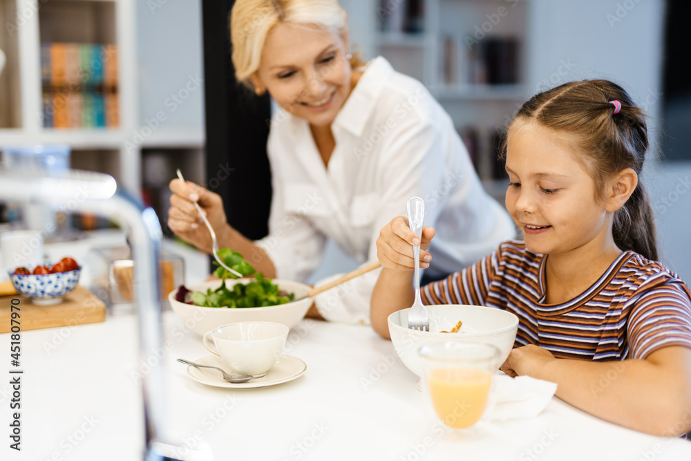 White mother and daughter smiling while having lunch in kitchen at home White mother and daughter smiling while having lunch in kitchen at home