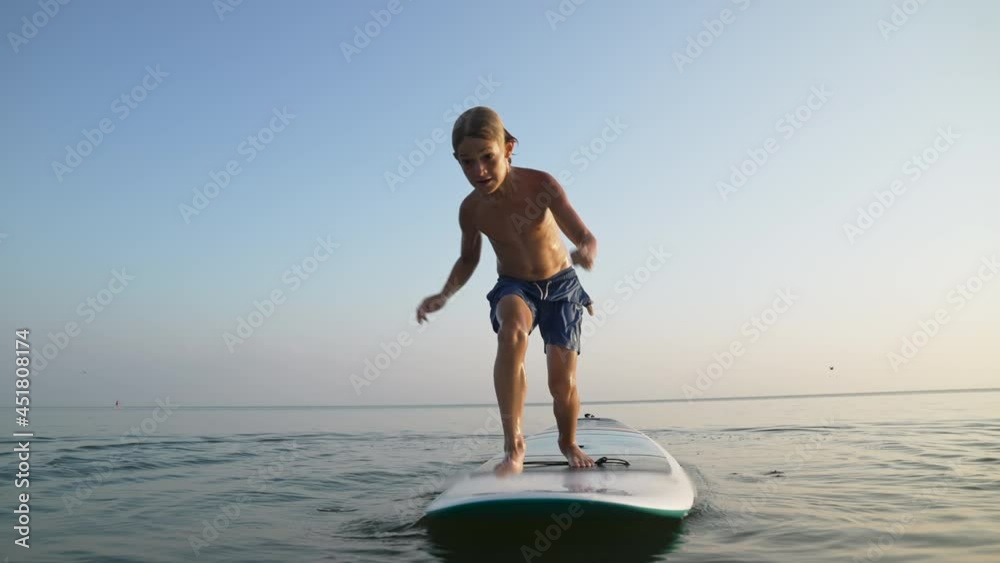 Happy child enjoying time in vacation on sea beach. Boy funny jumping to water from board on travel holiday at sunset.