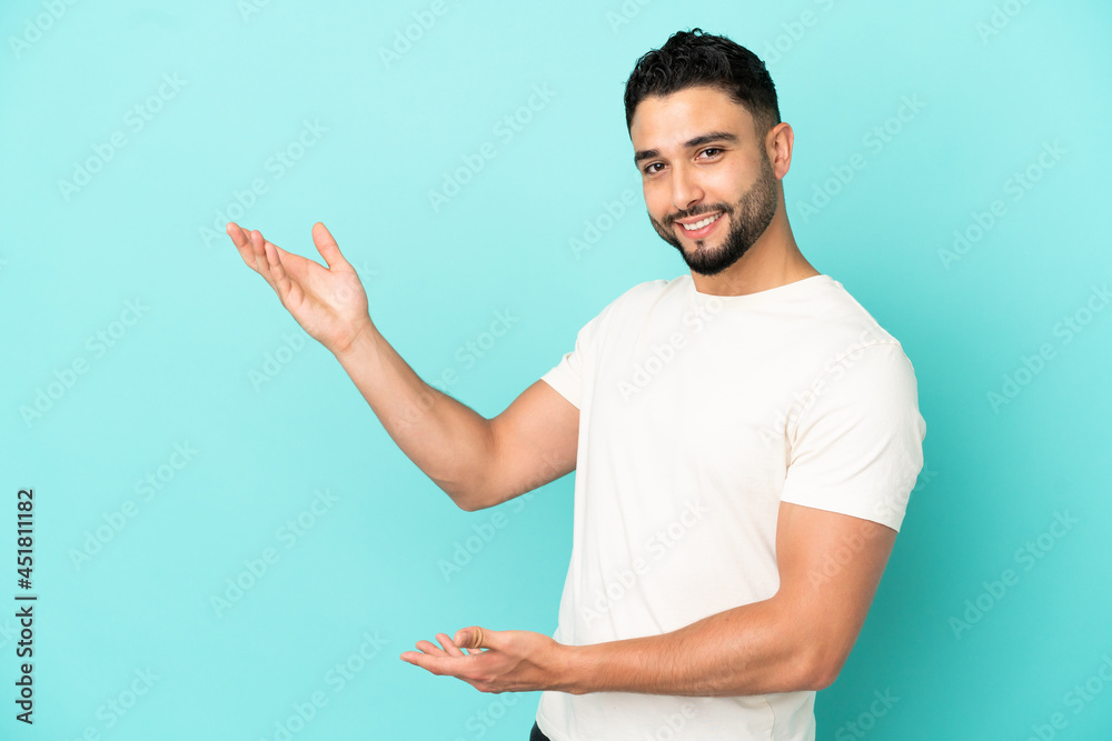 Young arab man isolated on blue background extending hands to the side for inviting to come Young arab man isolated on blue background extending hands to the side for inviting to come