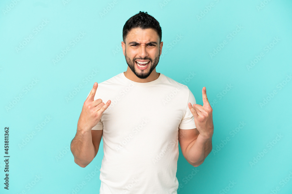 Young arab man isolated on blue background making horn gesture