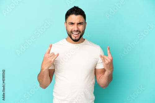 Young arab man isolated on blue background making horn gesture