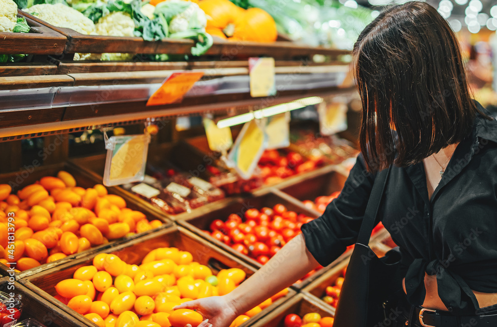 Woman chooses and purchases fresh ripe organic tomatoes in vegetable department of supermarket