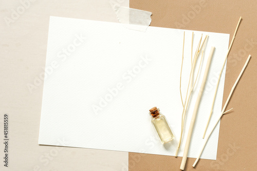 Top view of essential oils in a small transparent glass bottles and diffuser reeds sticks placed on blank white mock up card placed on beige and brown background, copy space. photo