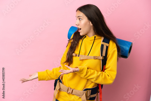Young mountaineer girl with a big backpack isolated on pink background with surprise expression while looking side