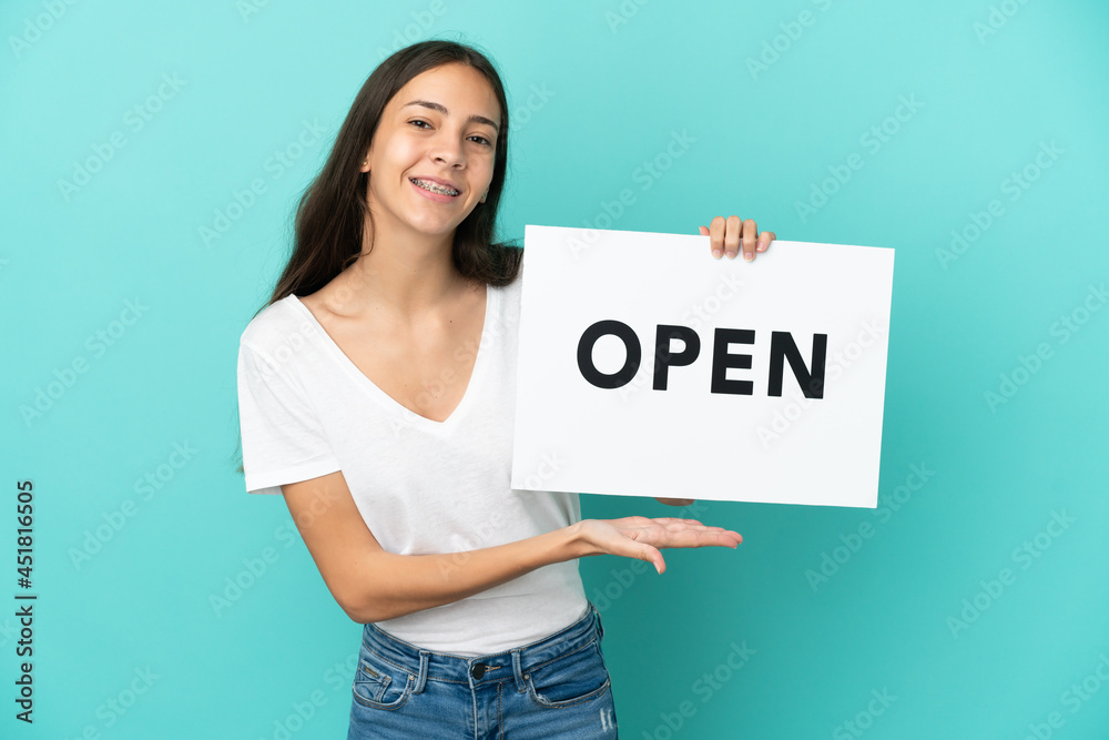 Young French woman isolated on blue background holding a placard with text OPEN with happy expression Young French woman isolated on blue background holding a placard with text OPEN with happy expression