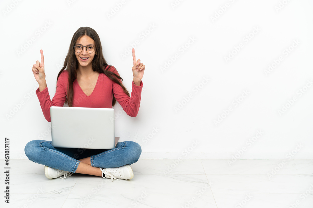 Young French girl sitting on the floor with her laptop pointing up a great idea Young French girl sitting on the floor with her laptop pointing up a great idea