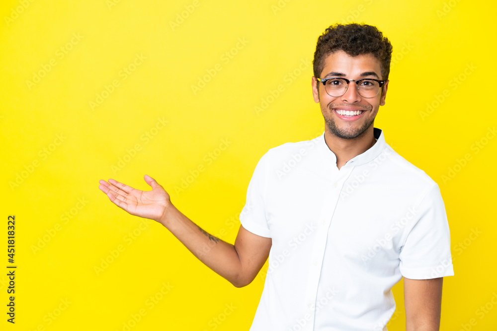 Young handsome Brazilian man isolated on yellow background extending hands to the side for inviting to come Young handsome Brazilian man isolated on yellow background extending hands to the side for inviting to come