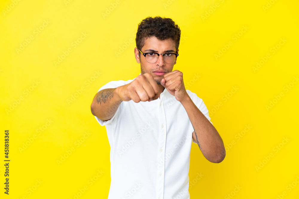 Young handsome Brazilian man isolated on yellow background with fighting gesture Young handsome Brazilian man isolated on yellow background with fighting gesture
