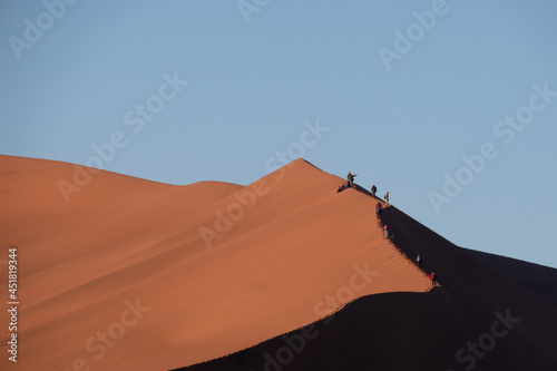 Tourists walking on the edge of a red sand dune at Sossusvlei National Park, a popular tourist destination in Namibia