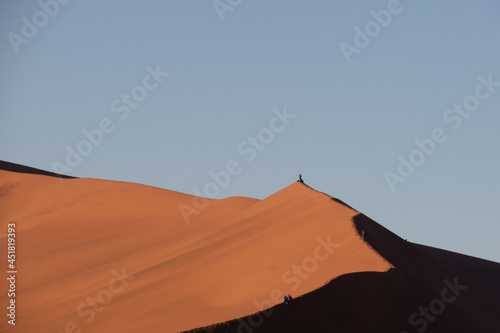 Tourists walking and sitting on the edge of a red sand dune at Sossusvlei National Park  a popular tourist destination in Namibia