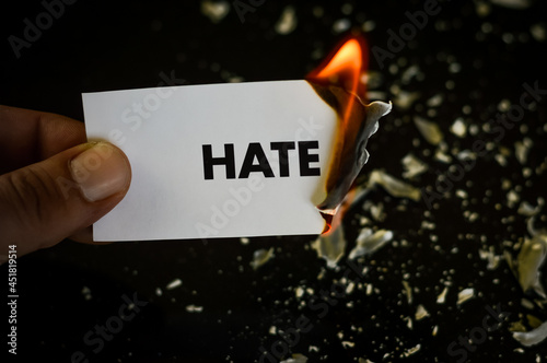 burning hate, human hand holding the word hate written on a paper burning with flame and ashes on a black background, concept
