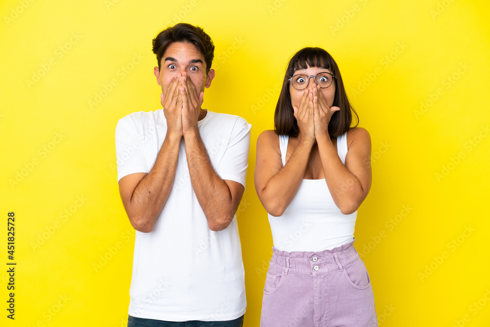 Young mixed race couple isolated on yellow background smiling a lot while covering mouth Young mixed race couple isolated on yellow background smiling a lot while covering mouth