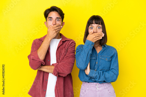 Young mixed race couple isolated on yellow background covering mouth with hands for saying something inappropriate