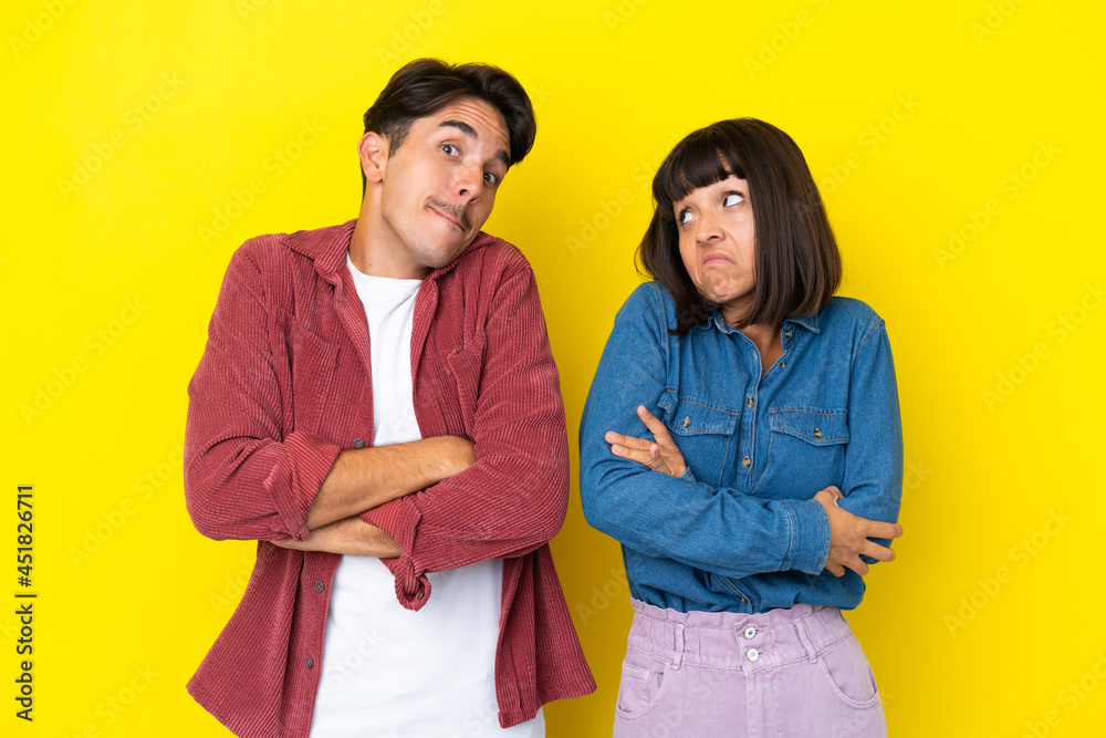 Young mixed race couple isolated on yellow background making doubts gesture while lifting the shoulders Young mixed race couple isolated on yellow background making doubts gesture while lifting the shoulders