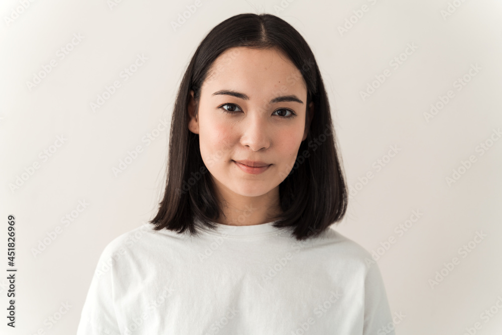Attractive asian girl wearing white t shirt looking straight into the camera. Young woman posing on a white wall background Attractive asian girl wearing white t shirt looking straight into the camera. Young woman posing on a white wall background