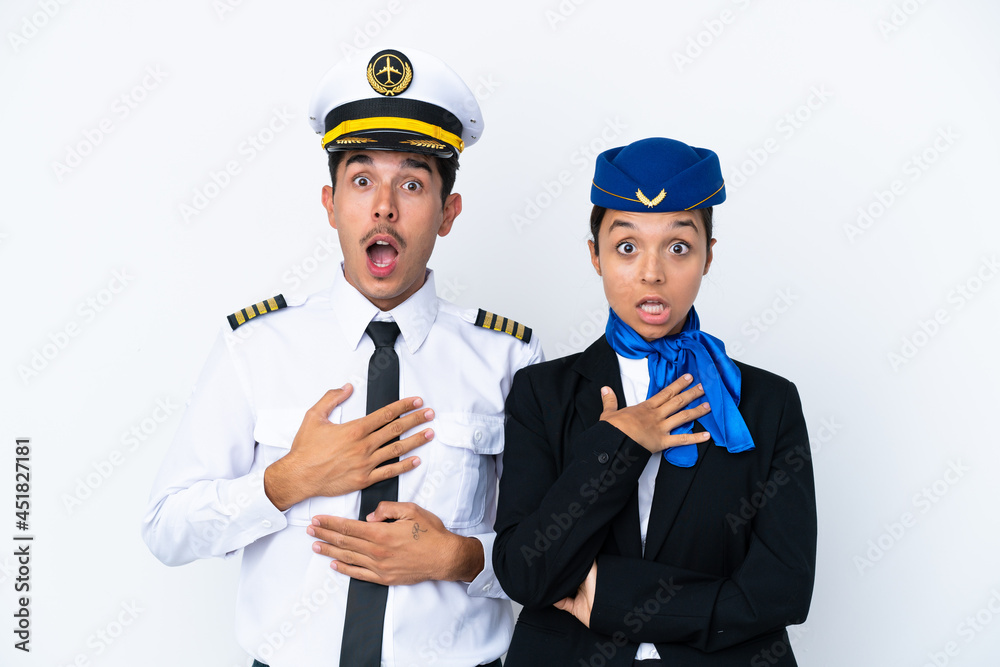 Airplane pilot and mixed race air hostess isolated on white background surprised and shocked while looking right Airplane pilot and mixed race air hostess isolated on white background surprised and shocked while looking right