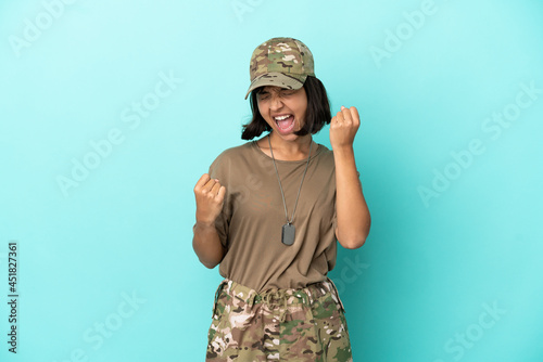 Military mixed race woman with dog tag isolated on blue background celebrating a victory