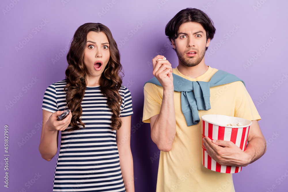 Photo of shocked excited couple wear casual clothes 3d spectacles holding tv remote eating pop corn isolated violet color background Photo of shocked excited couple wear casual clothes 3d spectacles holding tv remote eating pop corn isolated violet color background