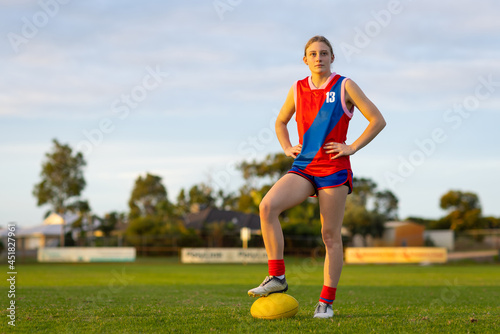 young female aussie rules footballer standing with hands on hips and foot on ball photo