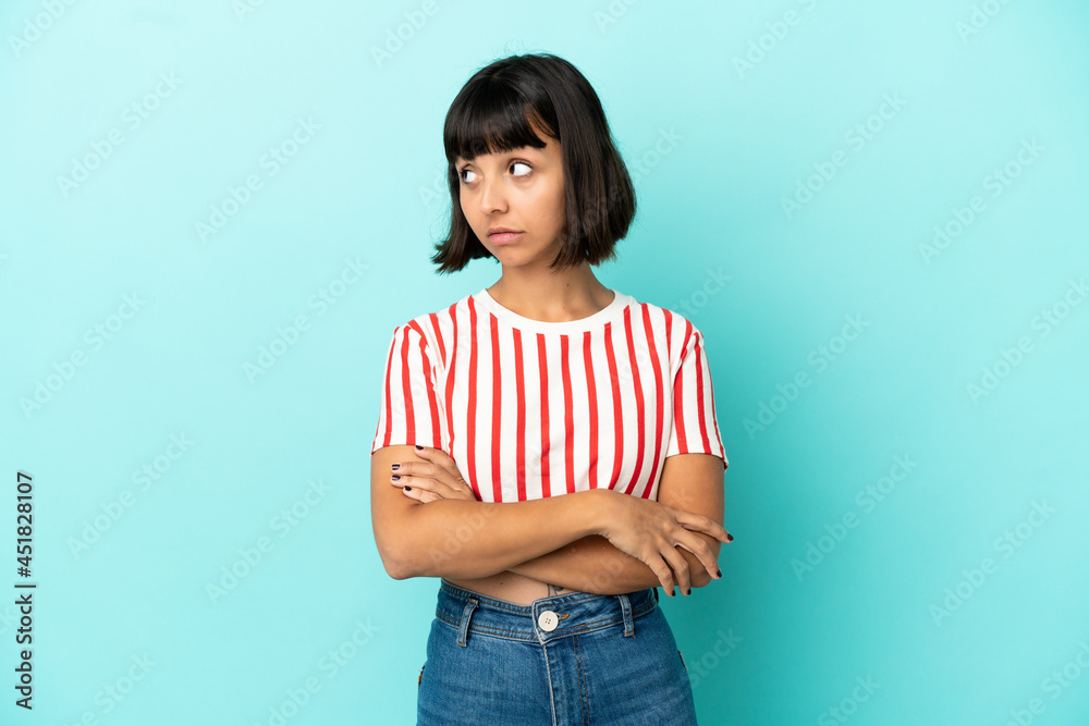 Young mixed race woman isolated on blue background making doubts gesture looking side Young mixed race woman isolated on blue background making doubts gesture looking side