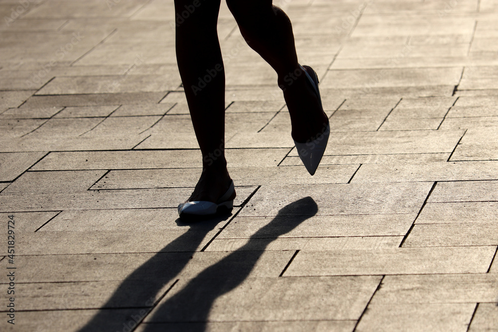 Silhouette and shadow of woman walking down on a street, female legs in pumps shoes