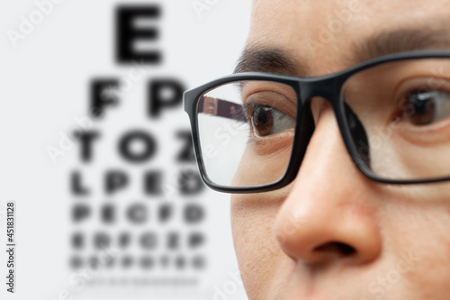 Portrait of a young man wearing eyeglasses with eye test chart isolated on white background