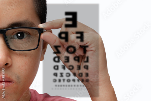 Portrait of a young man wearing eyeglasses with eye test chart isolated on white background. photo