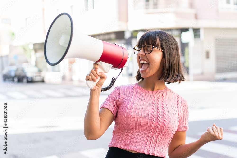 Young brunette woman in the city shouting through a megaphone to announce something in lateral position Young brunette woman in the city shouting through a megaphone to announce something in lateral position