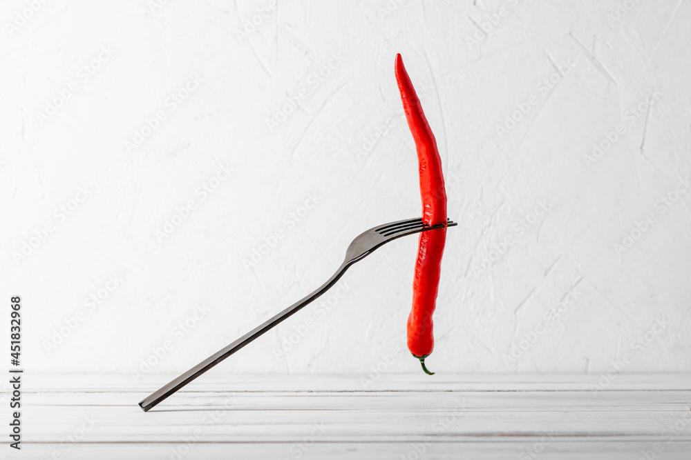 Red hot chili peppers on a fork on a white wooden background. Spicy food concept.