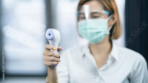 Close-up shot of doctor wearing protective mask ready to use infrared forehead thermometer (thermometer gun) to check body temperature for virus symptoms - epidemic virus outbreak concept