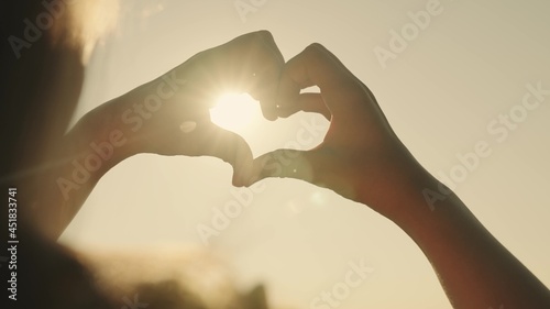 A girl shows her heart with her hands at sunset, a tourist trip, a romantic health vacation, dreaming to love life, an active lifestyle, a dream of a happy relationship with a loved one
