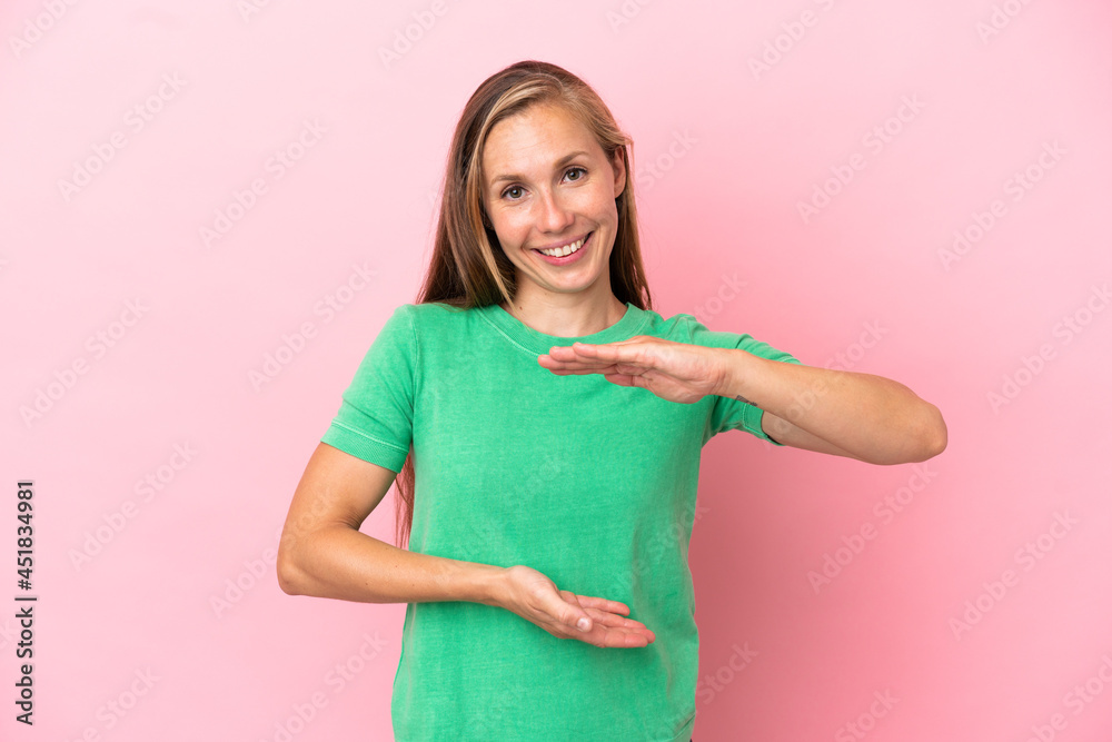 Young English woman isolated on pink background holding copyspace imaginary on the palm to insert an ad Young English woman isolated on pink background holding copyspace imaginary on the palm to insert an ad
