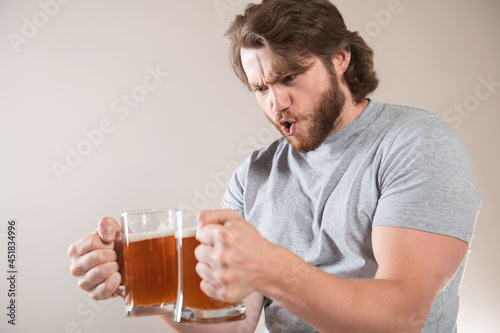 Portrait of a happy young bearded man holding two beer mugs isolated over light gray background