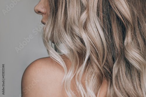 Close-up of the wavy blonde hair of a young blonde woman isolated on a gray background Fotobehang