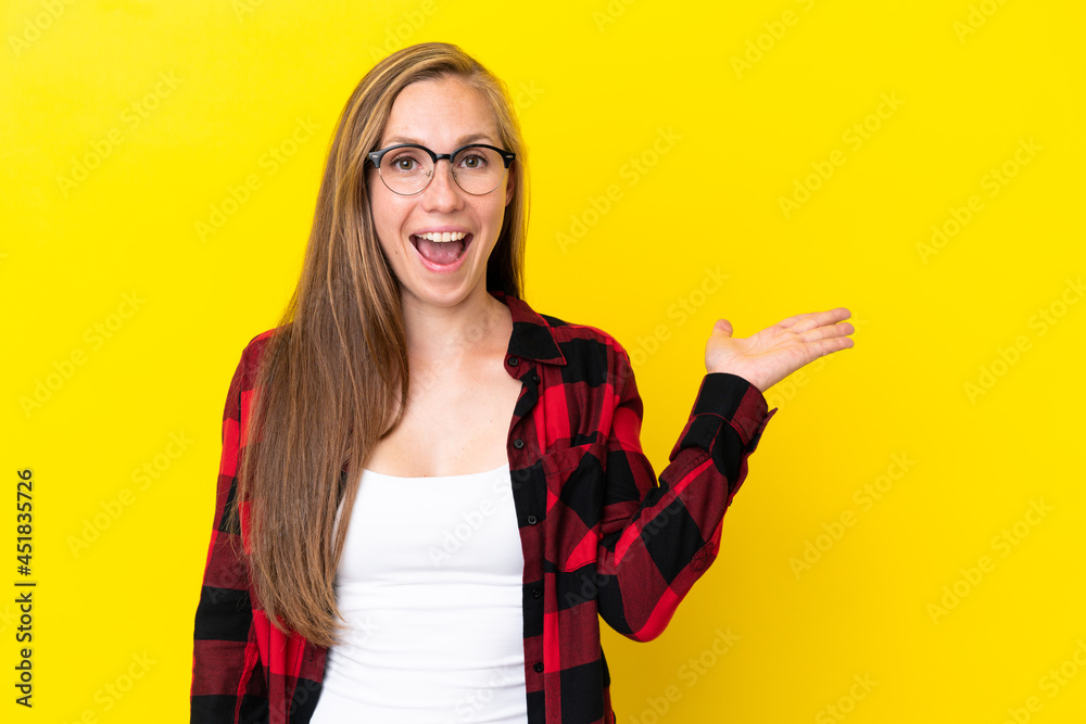 Young English woman isolated on yellow background holding copyspace imaginary on the palm to insert an ad Young English woman isolated on yellow background holding copyspace imaginary on the palm to insert an ad