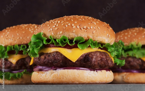 Three juicy tasty burgers close-up with salad and meat on dark background